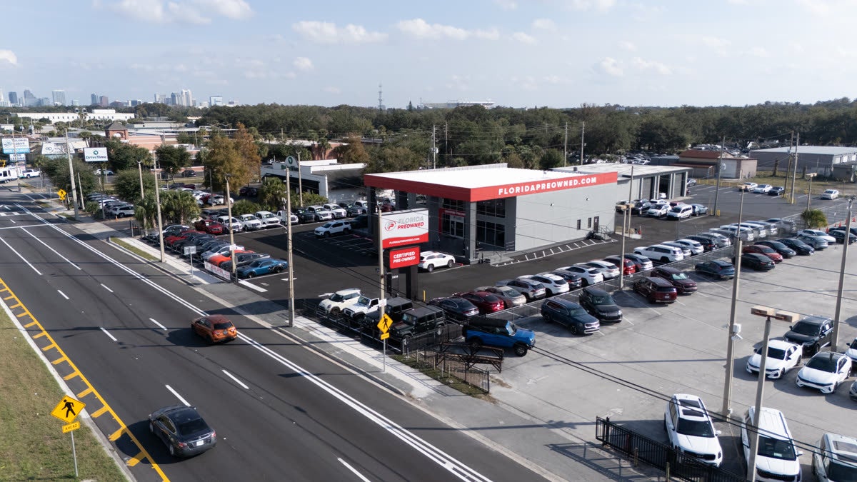 Aerial view of Florida Preowned dealership at 3450 W Colonial Drive, Orlando, FL 32808 — full pre-owned inventory lot with the Florida Preowned branded building and Orlando skyline in the background, 10 miles south of Altamonte Springs.